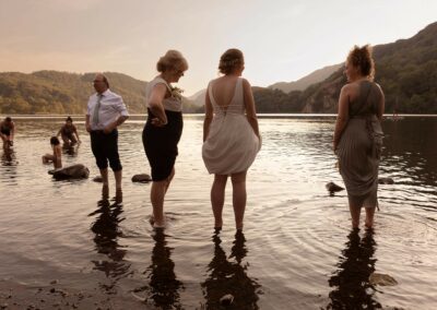 three woman scooping their skirts up whilst paddling in a lake by Anglesey wedding photographer Gill Jones photography