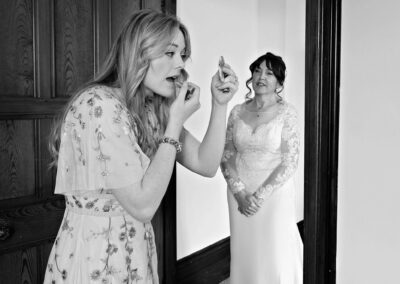 Bride watching her daughter apply lipstick to herself by Anglesey wedding photographer Gill Jones Photography