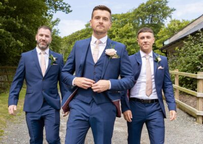 Groom buttoning up his jacket with this two groomsmen following behind him by Anglesey photographer Gill Jones Photography