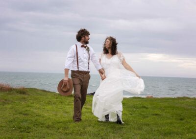 Bride and groom walking hand and hand on an island with the sea in the background at Cwyfan's Church by Anglesey Photographer Gill Jones Photography