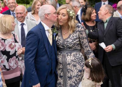 a groom goes to kiss his bride on her cheek a couple behind do the same to one another