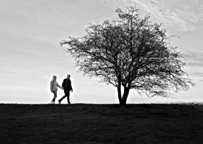 a silhouette of a man and woman walking towards a lone tree