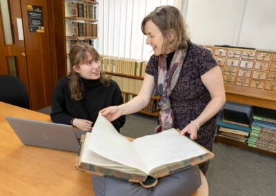 a library archivist turns the pages of a book as a student looks on by north wales commercial photographer Gill Jones Photography