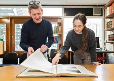 a student points towards a page of a large book as her tutor turns the page by north wales commercial photographer Gill Jones Photography